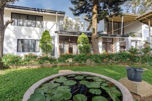 A modern two-story house with a well-maintained garden, including a pond with lily pads and flowering plants. - Grandeur 5bhk Villatheatre Hennurmanyata (Bengaluru)