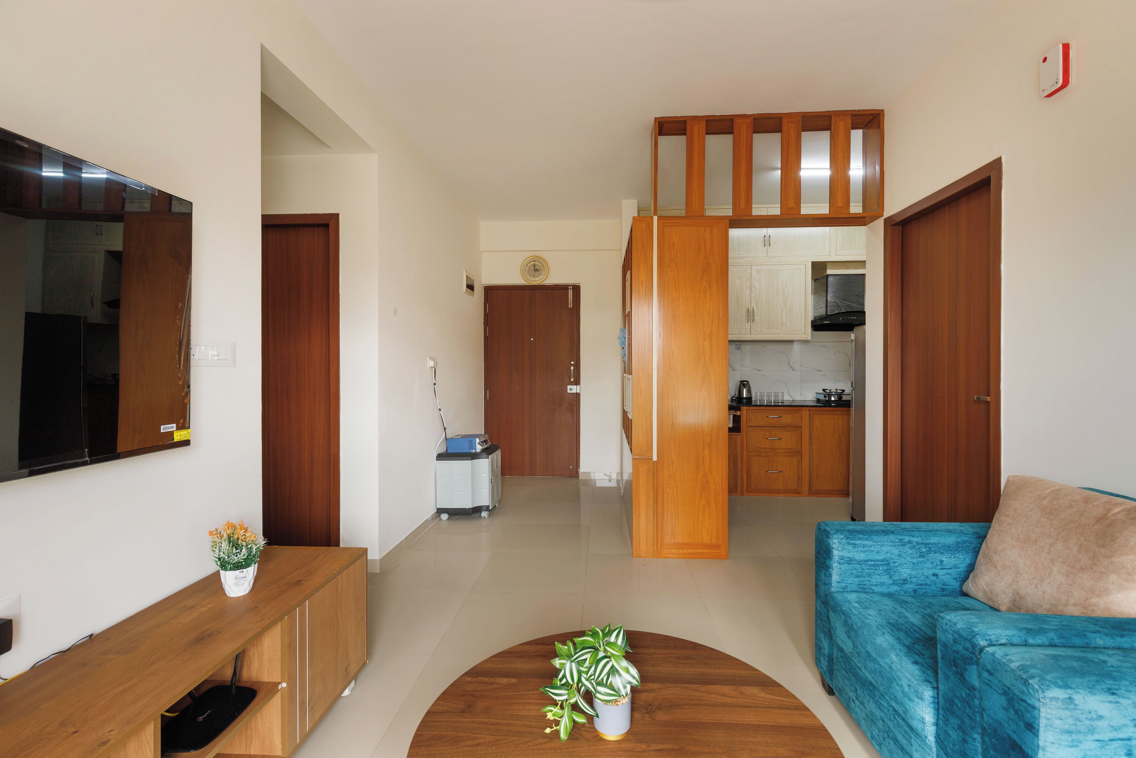 A modern living room with a blue sofa, wooden cabinets, a flat-screen TV, and a kitchen area in the background.