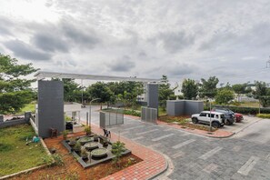 A parking area with a gated entrance, a small kiosk, and a paved walkway. - Lumara by Redolive 2bhk 20min E-city Nr Apollo (Anekal)