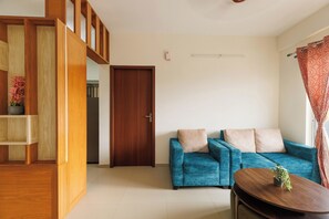 A living room with a blue sofa, a wooden cabinet, and a small table with a plant. - Lumara by Redolive 2bhk 20min E-city Nr Apollo (Anekal)