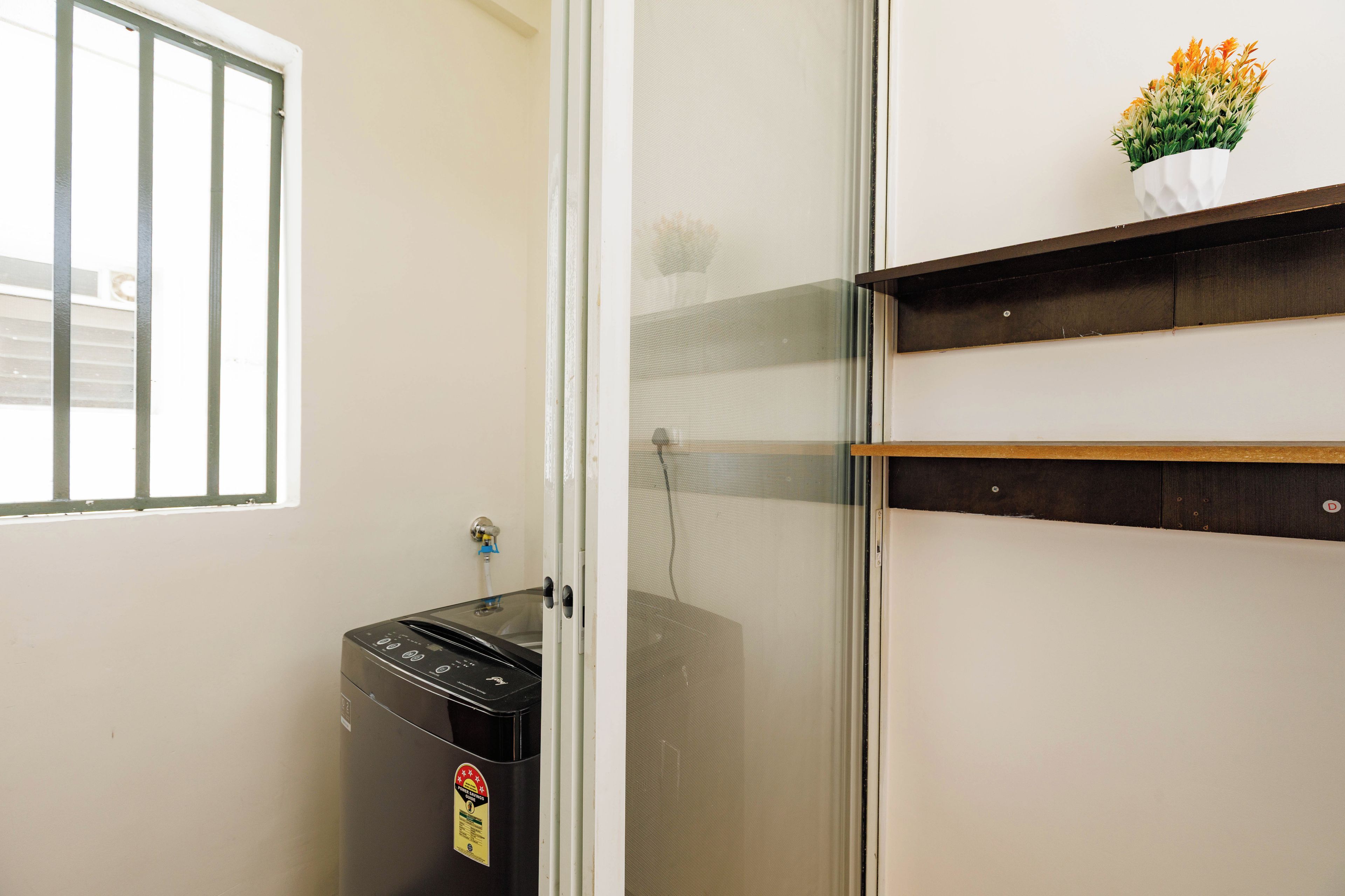 A kitchen with a dishwasher, a window with bars, and a small plant on a shelf.