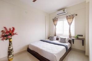 A bedroom with a bed, a nightstand, a potted plant, and a window with curtains. - Gladia by Redolive 1bhk Nr Manipal Whitefield (Bengaluru)