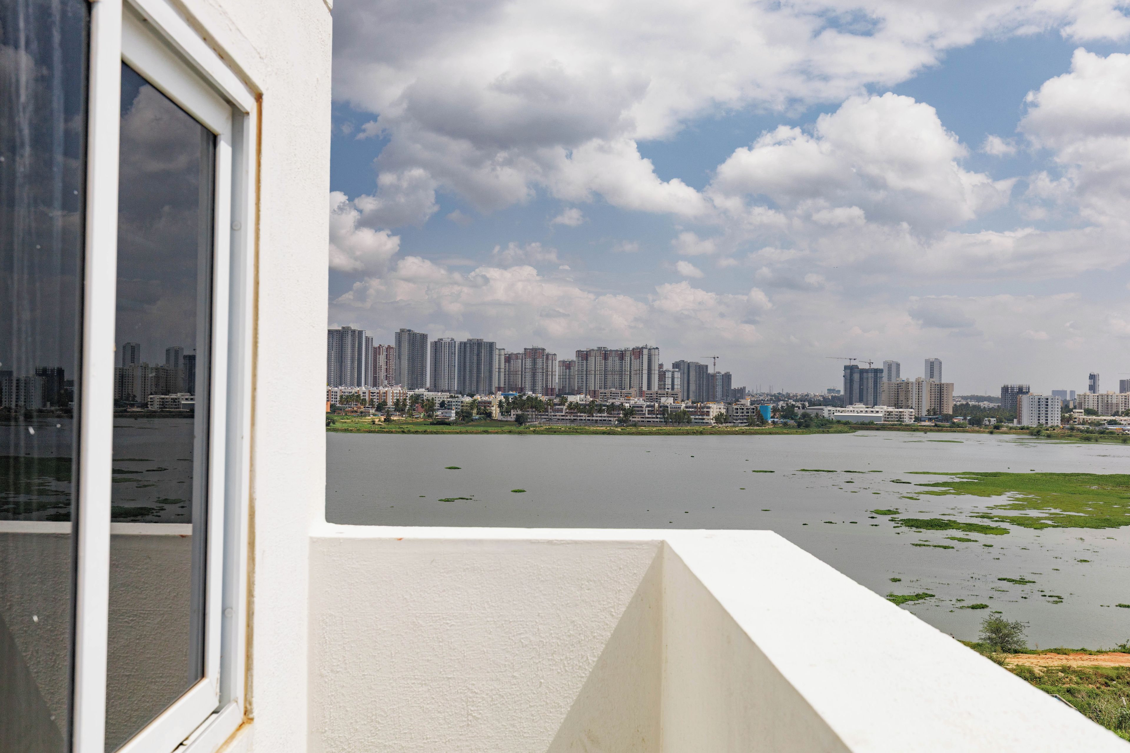 A view of a river with a cityscape in the background, a window on the left, and a white building in the foreground.