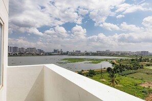 A balcony with a view of a city skyline, a river, and green fields. - Gladia by Redolive 1bhk Nr Manipal Whitefield (Bengaluru)