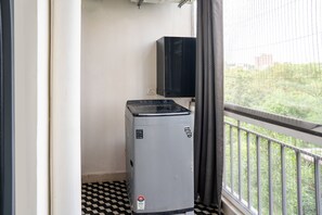 A compact room with a small refrigerator, a window with a view of greenery, and a checkered floor. - Belmont by Redolive 3bhk 30min DLF Cyber City (Sohna)