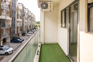 A narrow balcony with a green artificial turf, a glass railing, and a row of parked cars along the street. - Belmont by Redolive 3bhk 30min DLF Cyber City (Sohna)