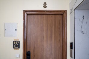 A wooden door with a brass handle, a wall-mounted elevator control panel, and a doorbell. - Belmont by Redolive 3bhk 30min DLF Cyber City (Sohna)