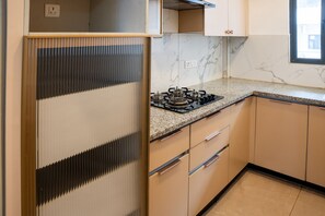 A kitchen with a gas stove, cabinets, and a window. - Belmont by Redolive 3bhk 30min DLF Cyber City (Sohna)