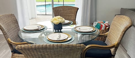 A dining area with wicker chairs, a glass table, and a view of a swimming pool.