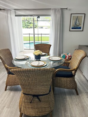 A dining area with wicker chairs, a glass table, and a view of a swimming pool. - Spacious 4-bedroom house with AC in beautiful Cape Coral (Cape Coral)