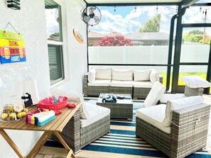 A covered outdoor seating area with wicker furniture, a table with drinks and snacks, and a sign indicating no working during certain hours. - Spacious 4-bedroom house with AC in beautiful Cape Coral (Cape Coral)