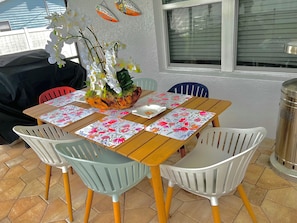 Eine Terrasse im Freien mit einem Holztisch, blumigen Untersetzern und Plastikstühlen.