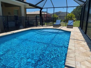 A swimming pool with a clear blue water surface, surrounded by a covered patio area with chairs and a view of the neighborhood. - Spacious 4-bedroom house with AC in beautiful Cape Coral (Cape Coral)