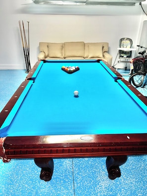 A pool table with a white cue ball, surrounded by a beige sofa and a bicycle. - Spacious 4-bedroom house with AC in beautiful Cape Coral (Cape Coral)
