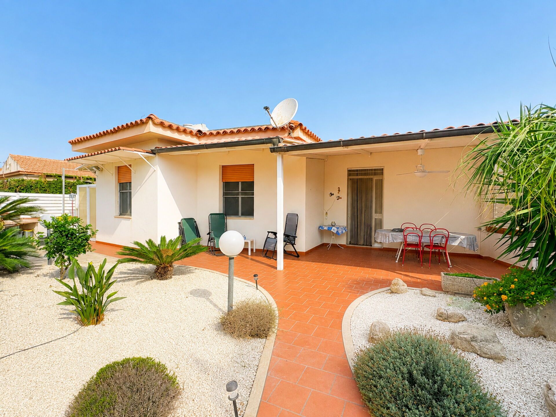 A residential property with a tiled patio, outdoor seating, and a satellite dish.