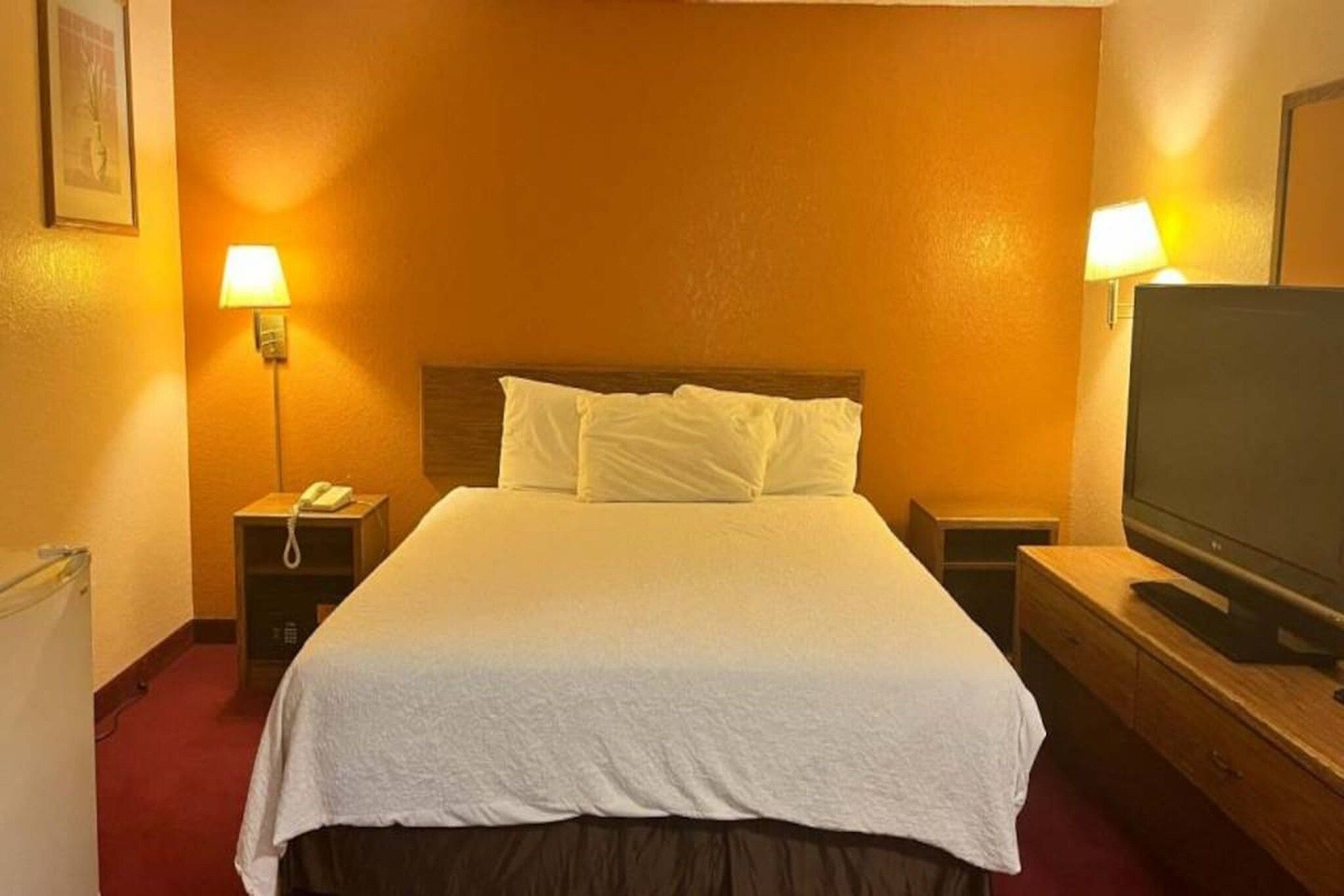 A hotel room with a bed, two bedside lamps, a telephone, a television, and a small table.