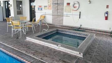 Una piscina con bordeado de baldosas, zona de estar con sillas y señales de seguridad en las paredes.