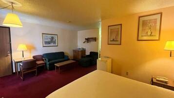 A hotel room with a bed, two chairs, a sofa, a small table, and two lamps.