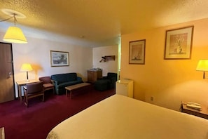 A hotel room with a bed, two chairs, a sofa, a small table, and two lamps.