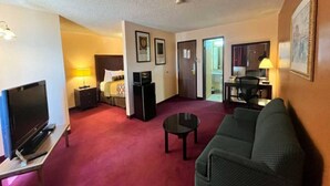 A hotel room with a television, a bed, a desk, a chair, and a sofa. - 1 King Bed | Non-Smoking, Micfridge (Deming NM)