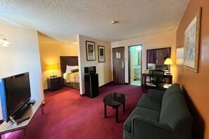 A hotel room with a television, a bed, a desk, a chair, and a sofa. - 1 King Bed | Non-Smoking, Micfridge (Deming NM)