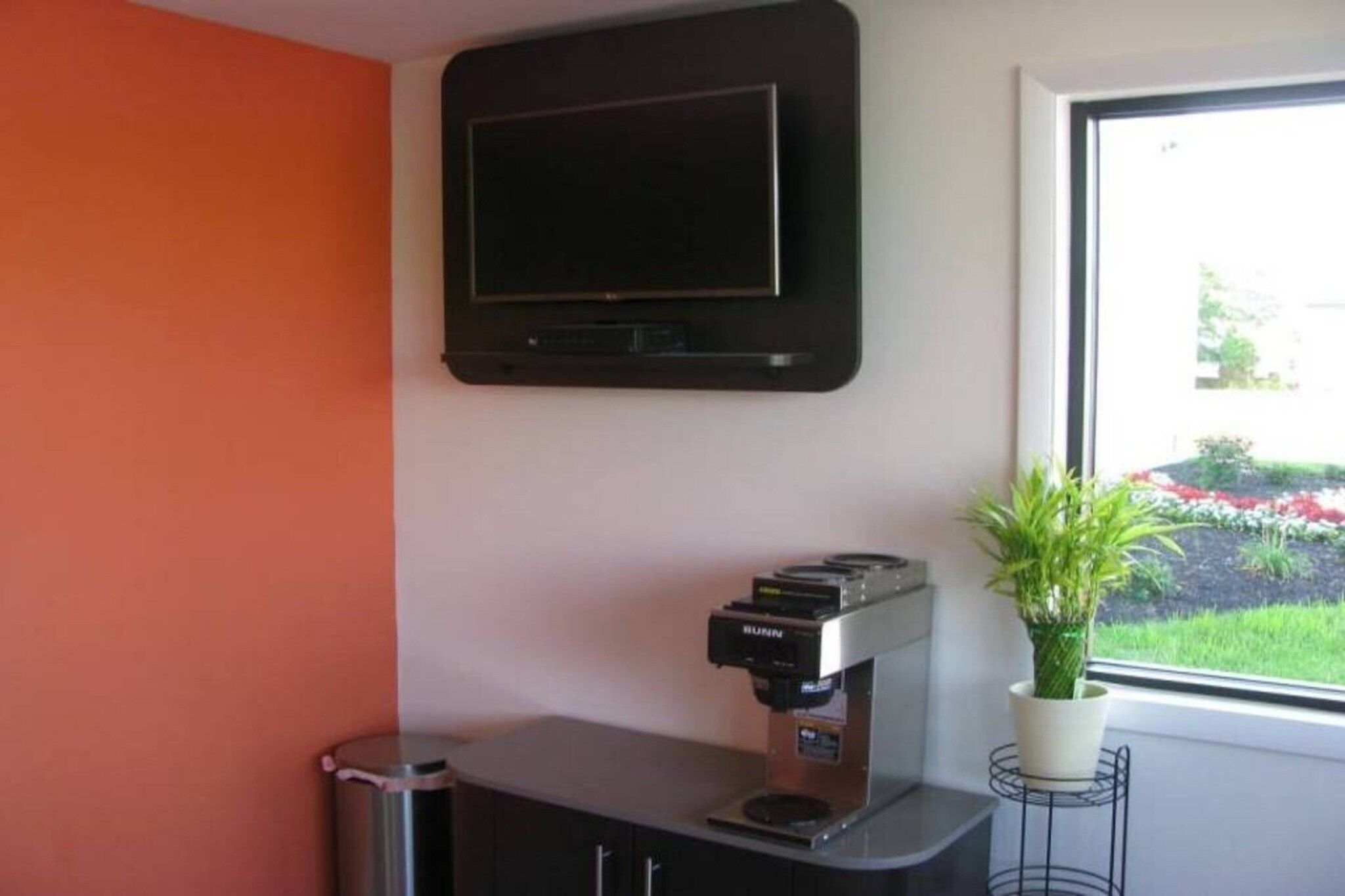 Habitación con televisión de pantalla plana en la pared, cafetera en la encimera y ventana con vistas a un jardín.