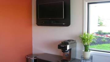 Habitación con televisión de pantalla plana en la pared, cafetera en la encimera y ventana con vistas a un jardín.