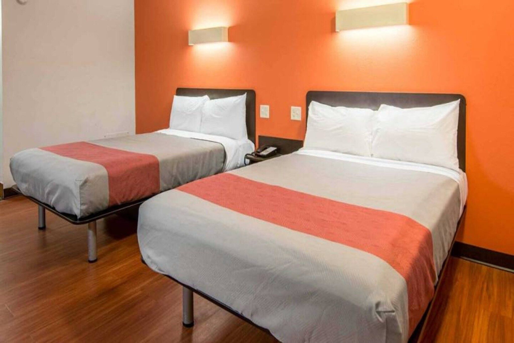 Two single beds with white and red bedding, wooden flooring, and orange walls.