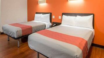 Two single beds with white and red bedding, wooden flooring, and orange walls.