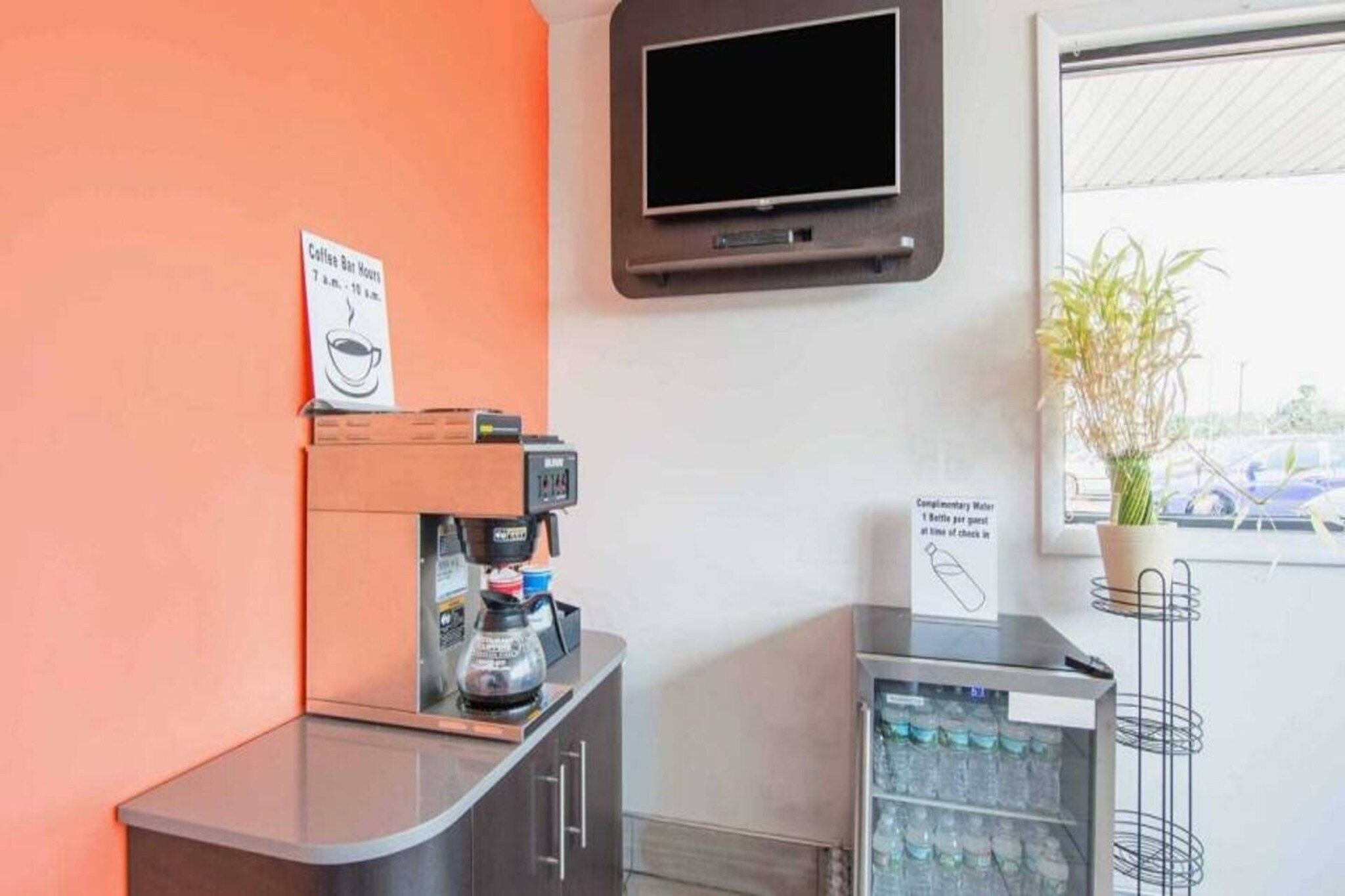 A coffee station with a coffee machine, a sign indicating complimentary water, and a television mounted on the wall.