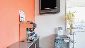 A coffee station with a coffee machine, a sign indicating complimentary water, and a television mounted on the wall.