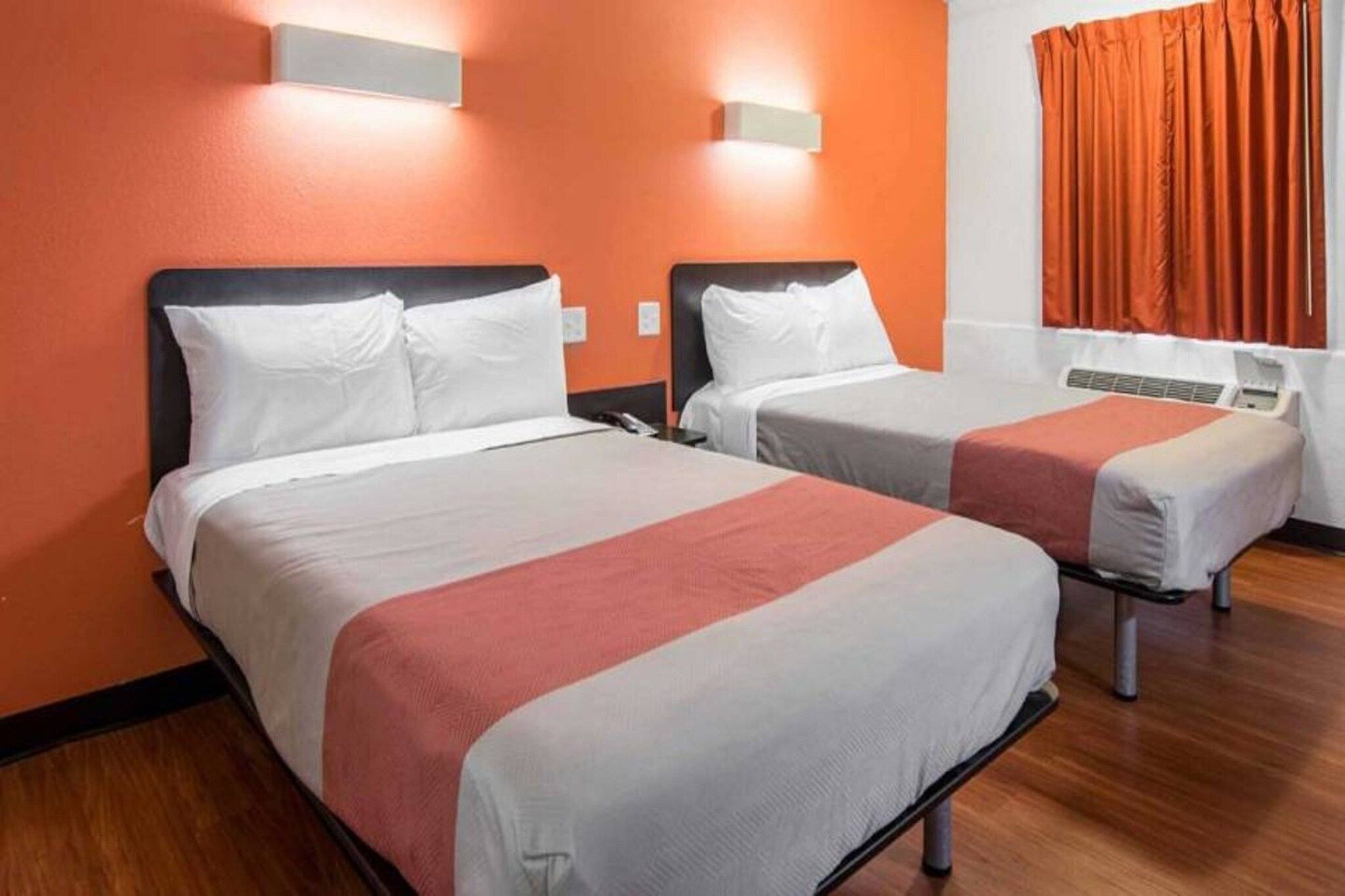 Ein Hotelzimmer mit zwei Betten, jeweils mit weißer Bettwäsche und roten Akzenten.