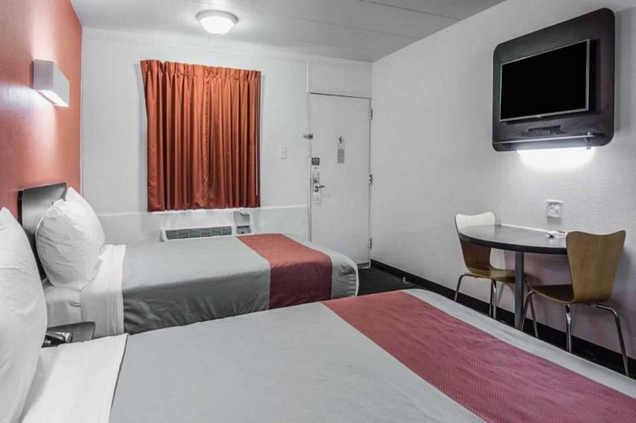 A hotel room with two beds, a desk, a chair, a television, and a window with curtains.