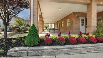 Un bâtiment doté d’une entrée abritée, d’un jardin aménagé avec différents arbustes et fleurs, et d’un ciel dégagé.