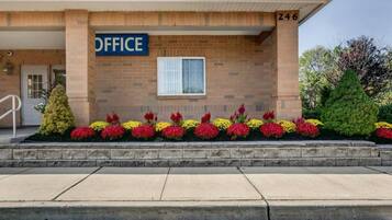 A building with a sign reading 'OFFICE' above the entrance, a brick facade, and a row of colorful flowers in front.