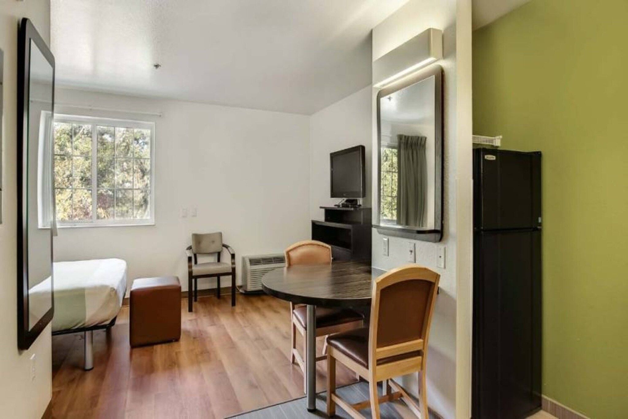 Una habitación compacta con una cama, una mesa de comedor con sillas, un televisor y un refrigerador.
