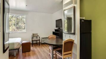 Una habitación compacta con una cama, una mesa de comedor con sillas, un televisor y un refrigerador.