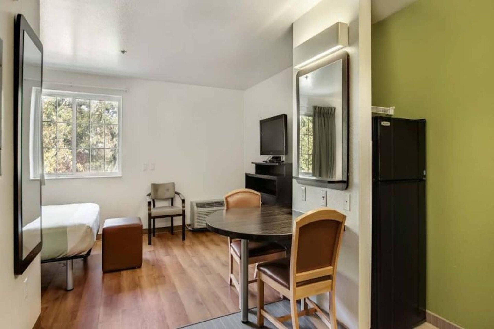 A room with a bed, a dining table with chairs, a TV, and a refrigerator.