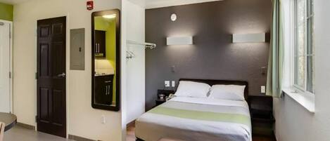 A hotel room with a bed, bedside table, lamp, and a mirror.