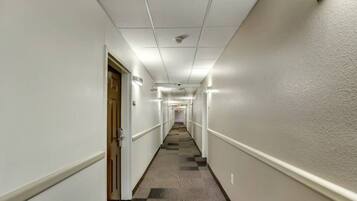 A long, narrow hallway with white walls and a carpeted floor, leading to a door at the end.