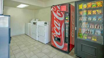 A room with a vending machine, a refrigerator, and stacked laundry machines.
