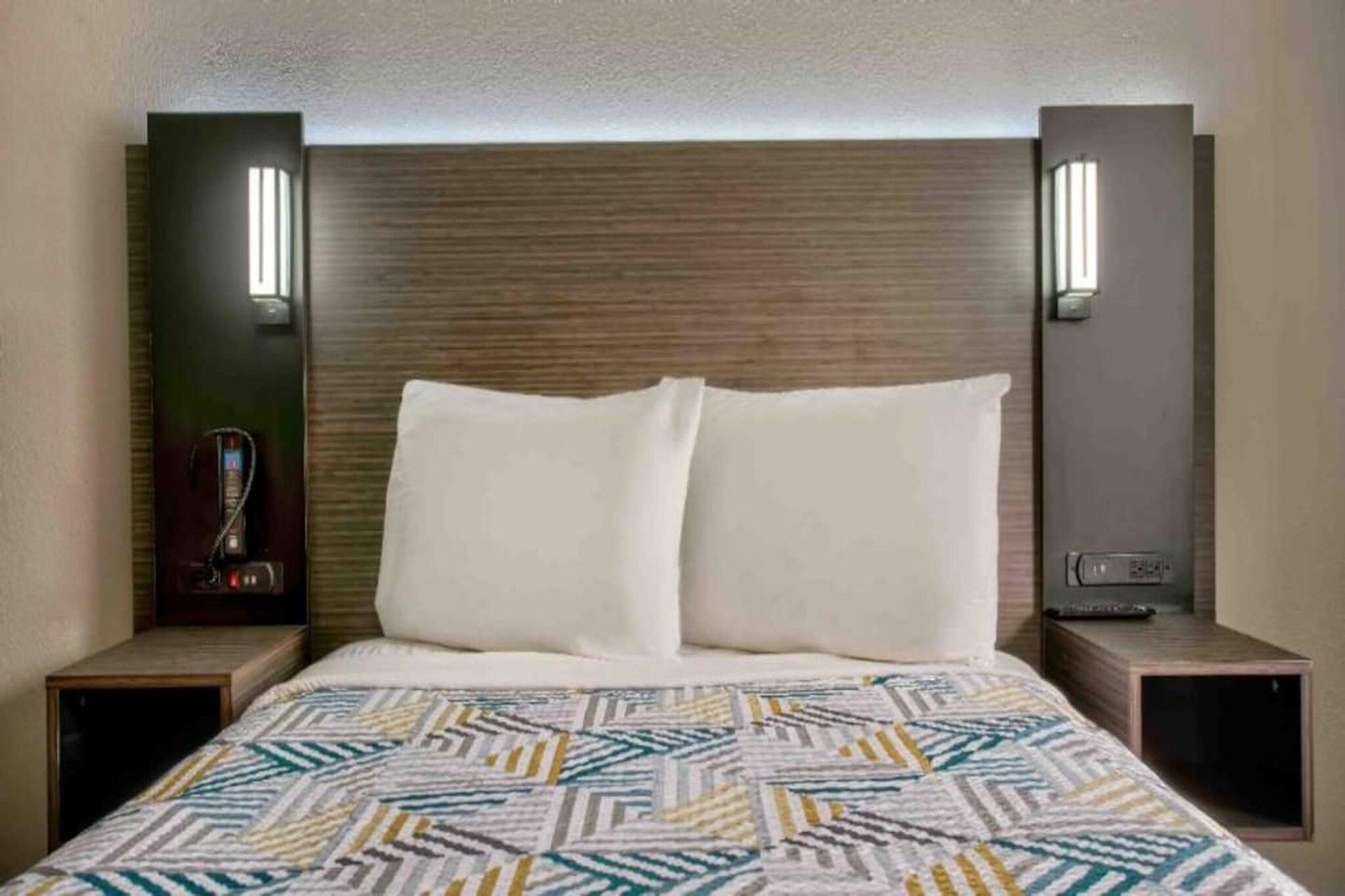A hotel room with a bed, two bedside tables, and wall-mounted lamps.