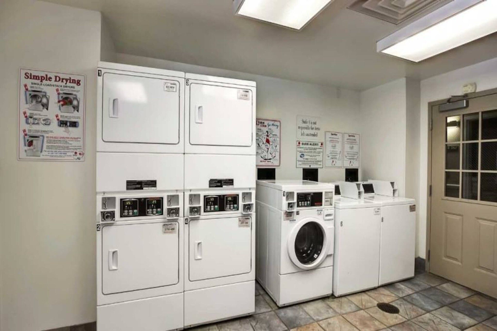 A laundry facility with stacked dryers and a front-loading washing machine.