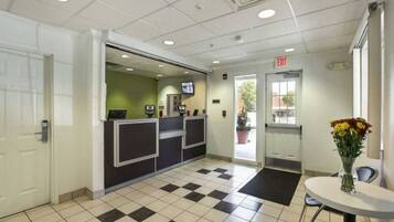 A reception area with a checkered floor, a reception desk, an exit sign, and a small table with a vase of flowers.