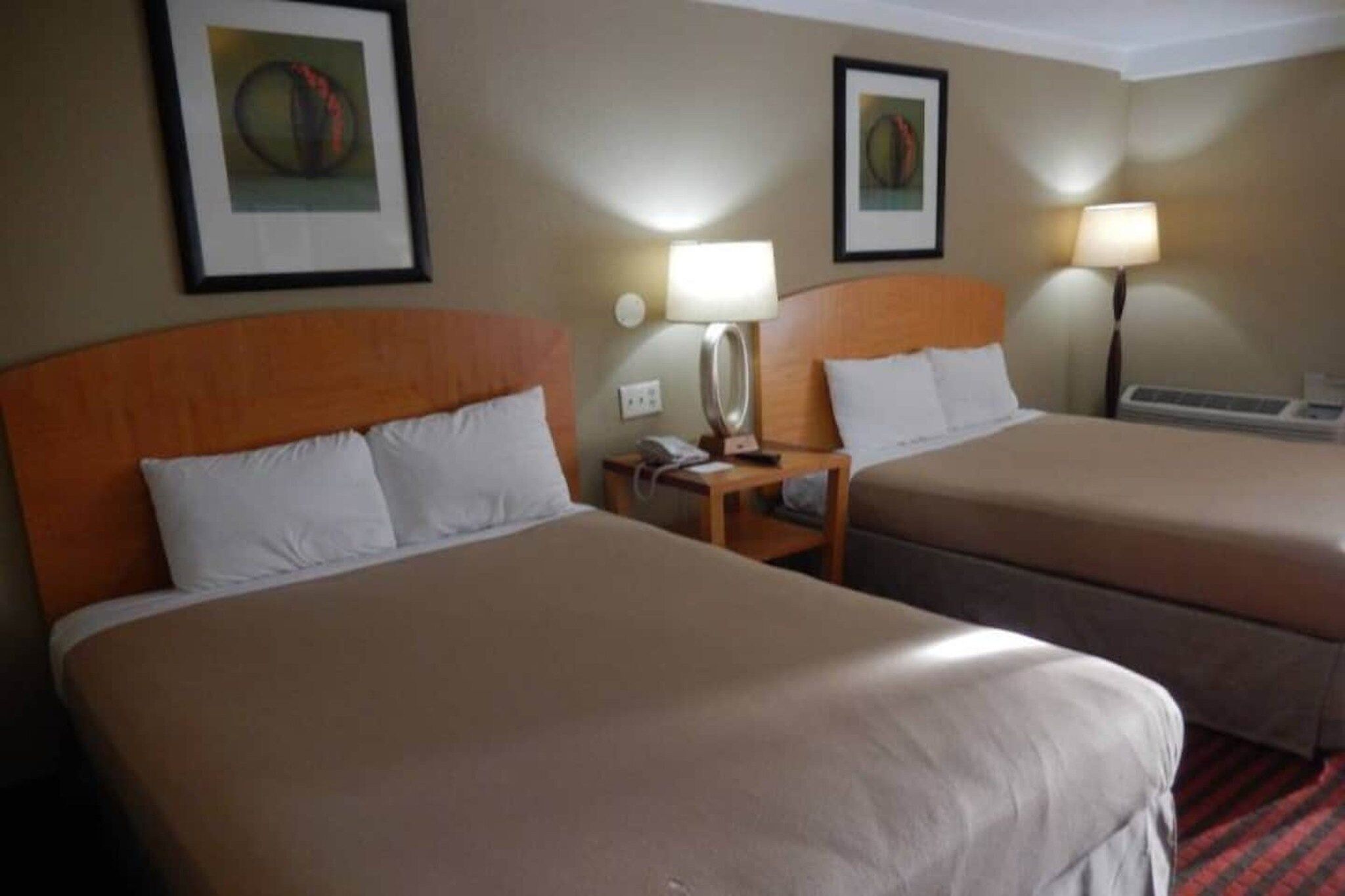 A hotel room with two beds, a nightstand with a lamp, and framed artwork on the walls.