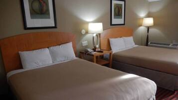 A hotel room with two beds, a nightstand with a lamp, and framed artwork on the walls.