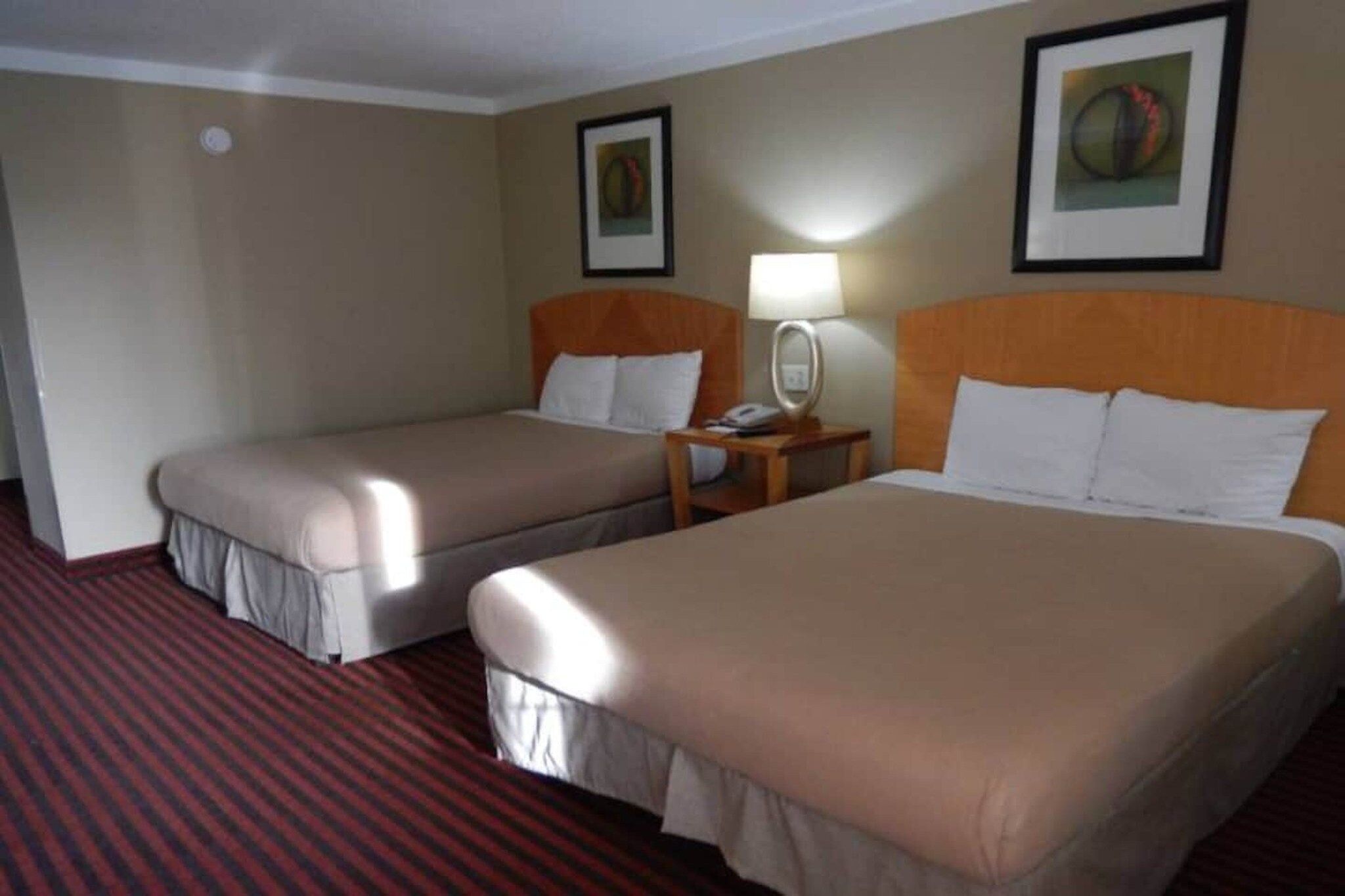 A hotel room with two beds, a nightstand with a lamp, and two framed pictures on the wall.