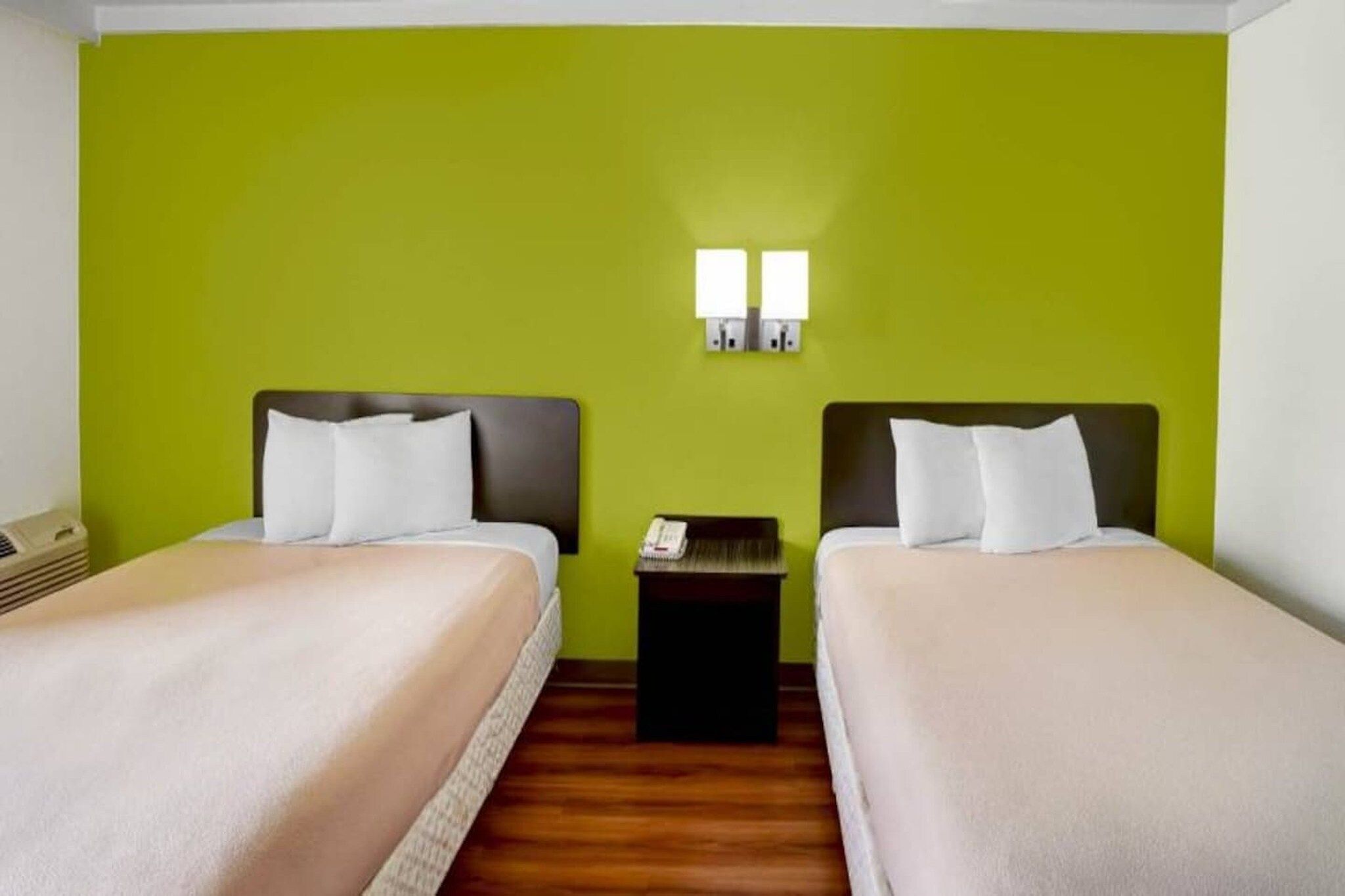 A hotel room with two beds, a nightstand, and a green wall.