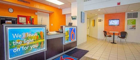 A hotel reception area with a digital display, a reception desk, and a seating area with chairs.