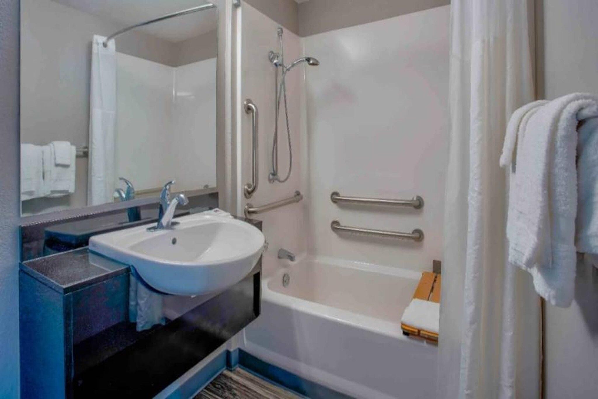 Ein Badezimmer mit Waschbecken, Spiegel, Dusche und Handtuchhalter.